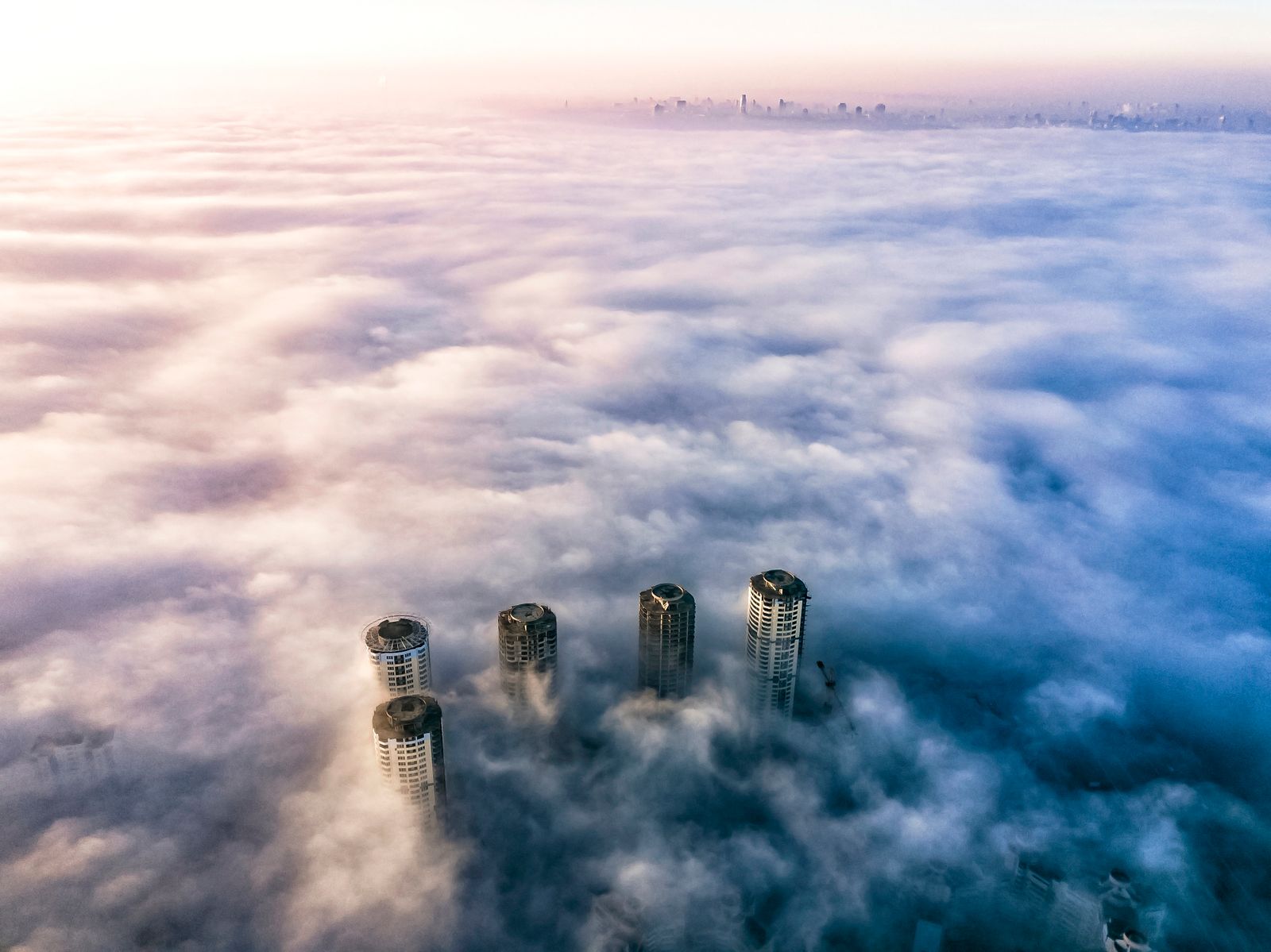 Aerial view of skyscrapers rising above a sea of low fog at dawn
